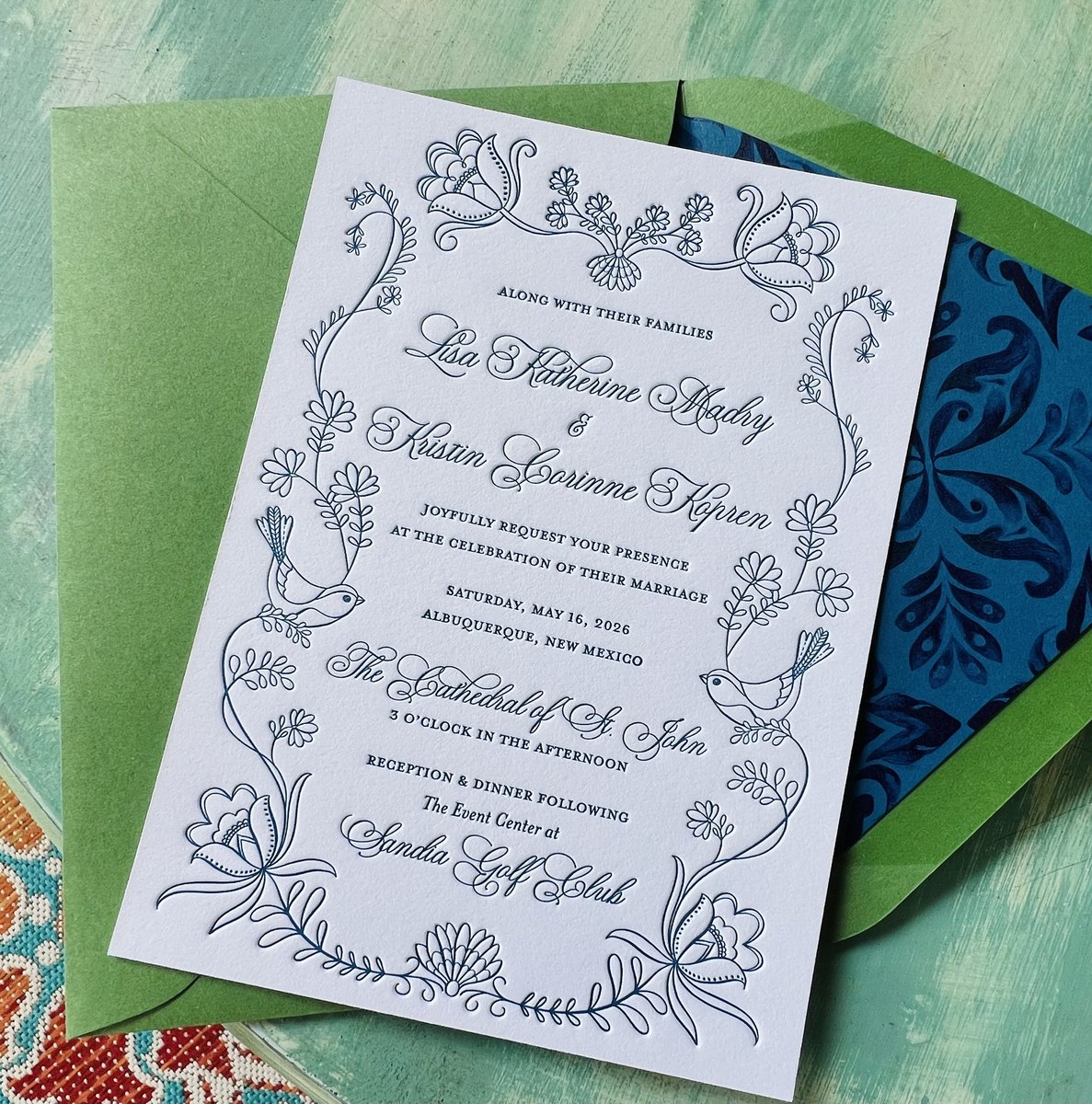 Letterpress wedding invitation in dusty blue line art with doves and wildflowers, on green and blue patterned envelopes